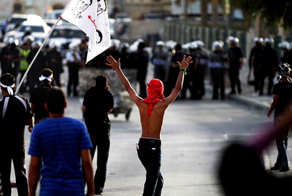 Bahraini anti-government protesters, one carrying a flag with images of a protester killed in earlier unrest, face off against riot police in Bilad al-Qadeem, Bahrain.