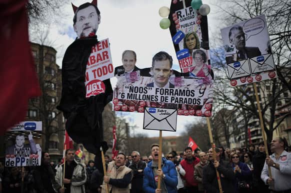A man carries a piece of cardboard with the portrait of Spanish PM Mariano Rajoy decorated as a devil, alongside portraits of Inaki Urdangarin, the Spanish`s king son-in-law and Former Popular Party`s treasurer, Luis Barcenas, during a protest against austerity in Pamplona northern Spain.