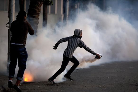 An Egyptian protester runs with a teargas canister during clashes with riot police, unseen, after protesters closed down a main street and jammed the traffic flow, in Cairo, Egypt.