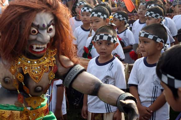 Balinese children react near a paper-mache effigy that symbolizes Balinese Hinduism’s mythical demons and monsters called ogoh ogoh during a parade to celebrate