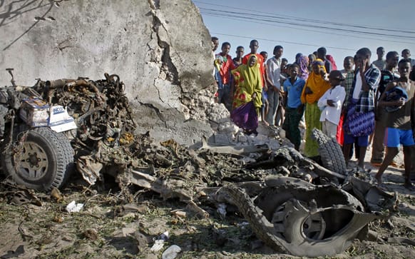 Somalis stand over the wreckage of a car following a blast at a restaurant near the beach in Mogadishu, Somalia.