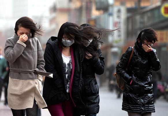Chinese women, some wearing face masks, brace through strong wind after the capital city is hit by sandstorm in Beijing.