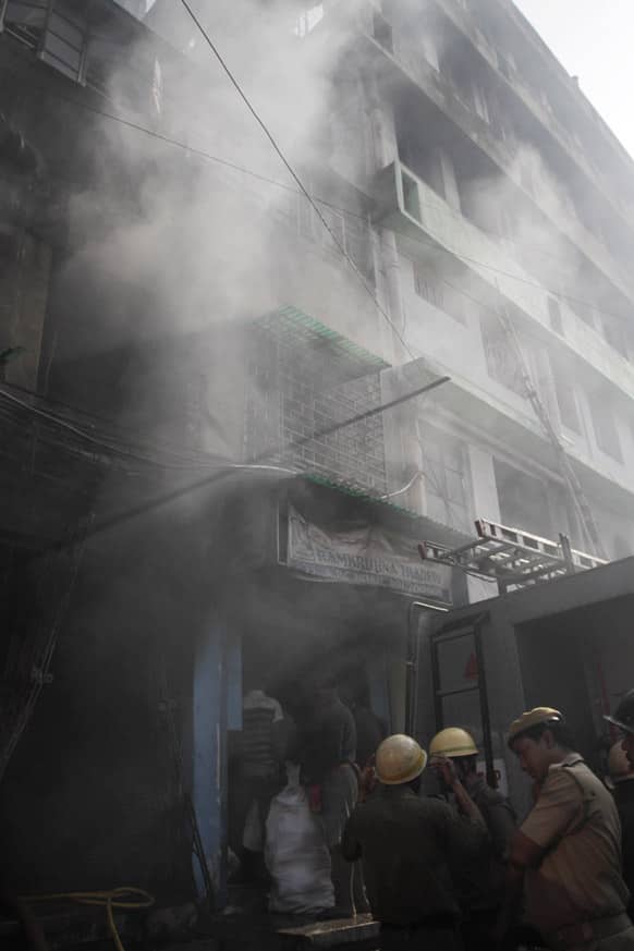 Firemen wait outside as smoke arises after a fire broke out early morning at an illegal six-story plastics market in Kolkata.
