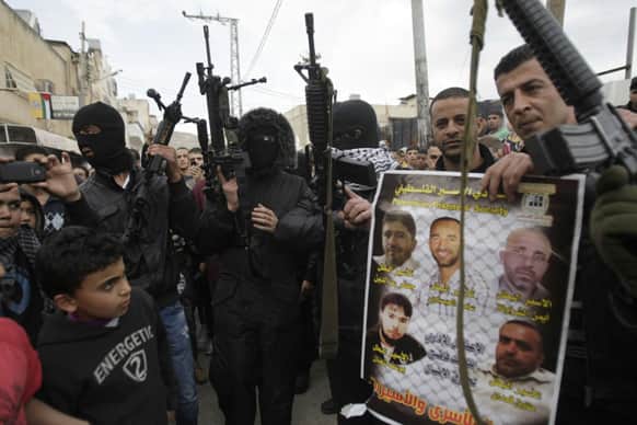 A man holds a poster showing imprisoned Palestinians as he is surrounded by armed militants in in the Balata refugee camp in the West Bank town of Nablus during a rally in support of Palestinian prisoners.