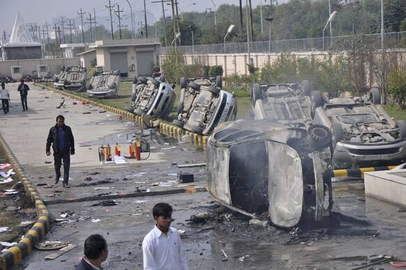 People walk past vandalized cars at the premises of a factory on the first day of a two day strike in Noida.