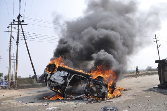A policeman runs past a burning car set on fire by vandals on the first day of a two-day strike in Noida.