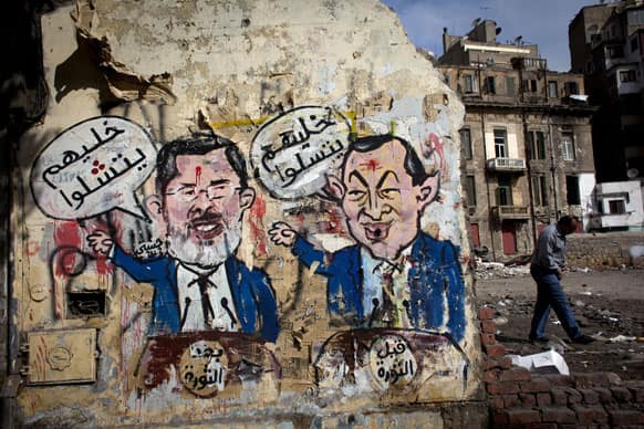 An Egyptian man walks by a mural depicting ousted president Hosni Mubarak, right, and Egyptian President Mohammed Morsi, left, with Arabic that reads