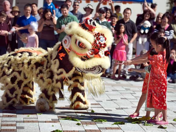 Three girls deliver red envelopes to the lion during the Lion Dance at a Lunar New Year celebration in Tustin, Calif.