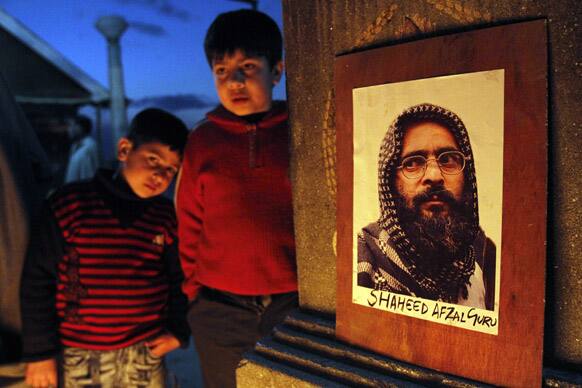 Kashmiri children stand next to a photograph of Mohammed Afzal Guru as students sit in a candle light protest demanding the return of his mortal remains to his family in Srinagar.