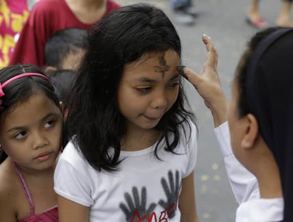 A Filipino Roman Catholic nun rubs the sign of the cross with ashes on the forehead of a worshiper in observance of