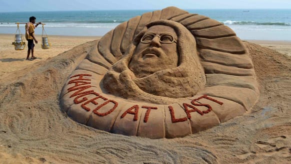 A snacks vendor walks past a sand sculpture of Kashmiri Mohammed Afzal Guru who was executed Saturday morning, at a beach in Puri.