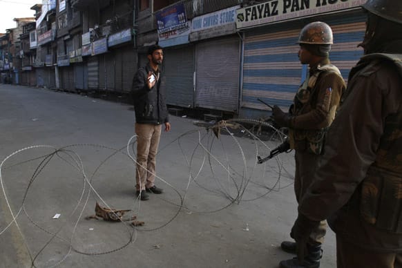 Paramilitary soldiers interrogate a civilian near a barbed wire set up as road blockade during curfew in Srinagar.