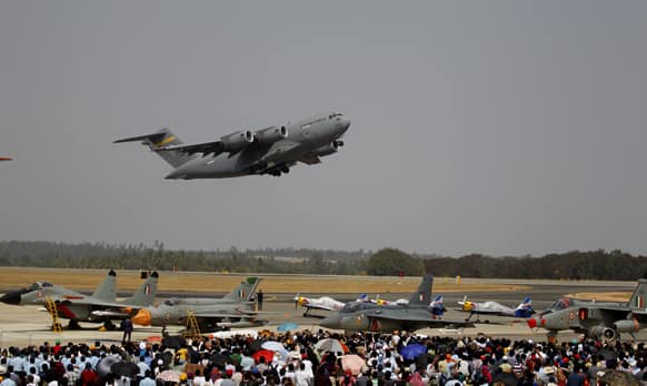 Visitors watch U.S. Air Force C-17 Globemaster III, a cargo plane, fly over other aircraft on the fourth day of the Aero India 2013 at Yelahanka air base in Bangalore.