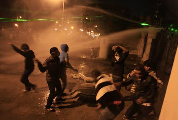 Egyptian protesters throw stones while security police open water canons on them from inside the grounds of the presidential palace during a demonstration in Cairo, Egypt.