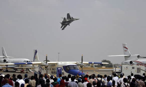 Visitors watch a Sukhoi Su-30 fighter aircraft fly over other aircraft on display on the third day of the Aero India 2013 at Yelahanka air base in Bangalore.