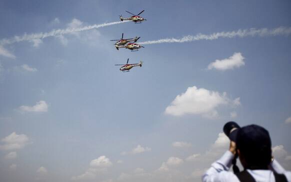 A photographer takes pictures of Indian Air Force helicopters as they perform aerobatic flight on the opening of the Aero India 2013 at Yelahanka air base in Bangalore.