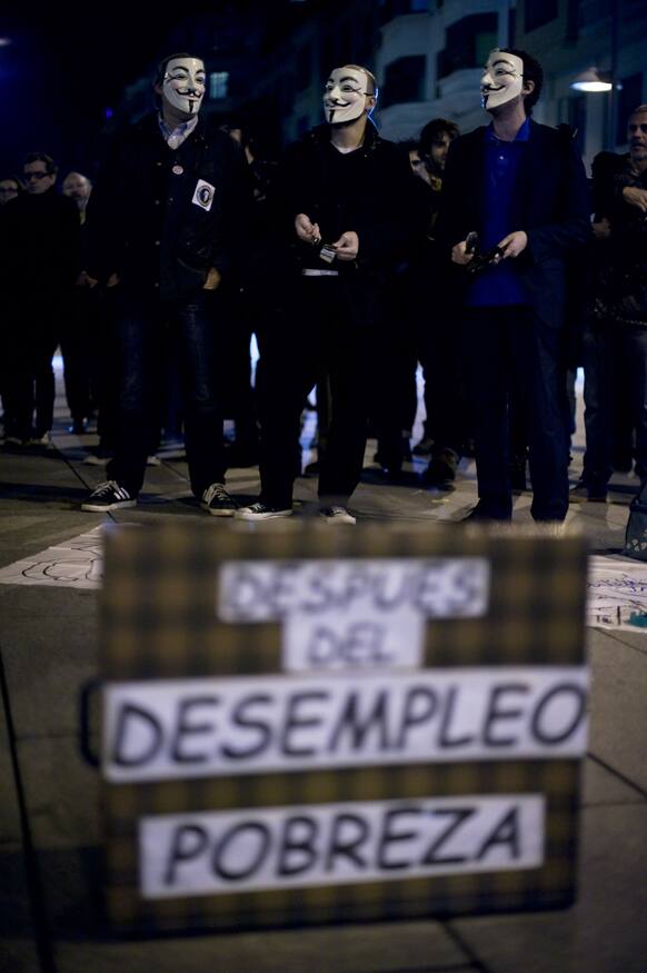 People cover their faces with masks as they protest next to Popular Party office, unseen, with a suitcase, front, reading, ``After unemployment, poverty``, in Pamplona, northern Spain.