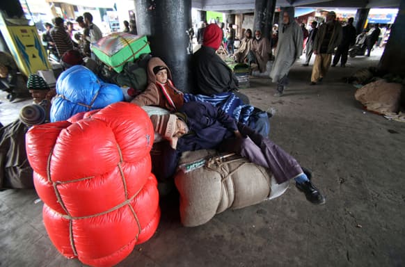 Stranded passengers rest on luggage as they wait for the Jammu-Srinagar highway to reopen at a bus station in Jammu.
