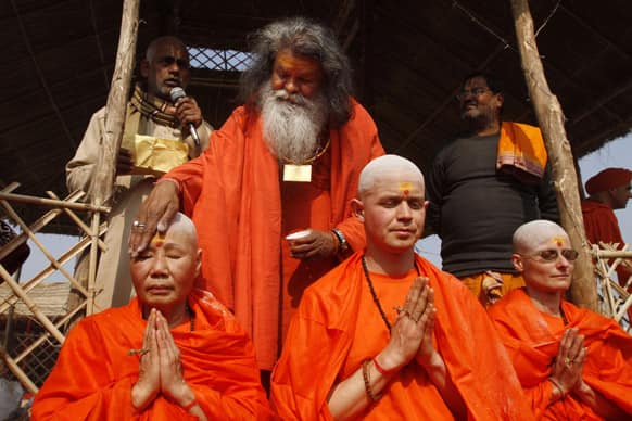 Chief priest of Mahanirvani Akhara, Swami Maheshwaranand Puri, applies ash to the forehead of Catherine Yutming of China as Juraj of Slovakia, center and Patricia of Czech Republic pray during their consecration ceremony as Brahmachari, or celibate during the Maha Kumbh festival, in Allahabad.