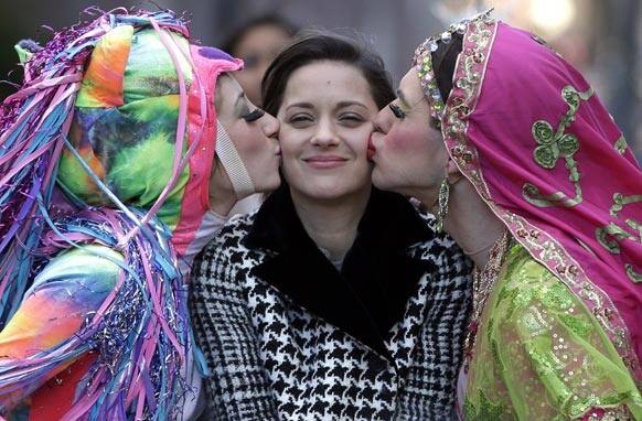 Actress Marion Cotillard, of France, center, the Hasty Pudding Woman of the Year, is kissed by Harvard University theatrical students Renee Rober, left, and Ben Moss, right, as they ride in the back of a convertible during a parade through Harvard Square, in Cambridge, Mass.