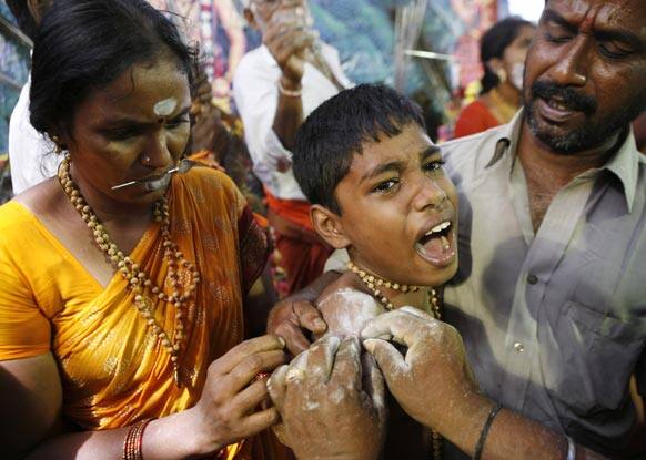 A young Hindu devotee reacts in pain as he gets his body pierced with a metal rod during the Thaipusam festival, in Chennai.
