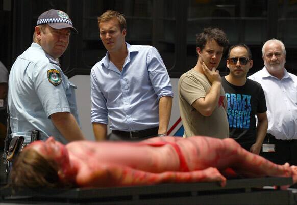 A police officer, left, and four other men watch as activist Zoe Crawford uses body paint to simulate seared flesh as she lays on a barbecue grill in Sydney, Australia, during a protest by PETA.