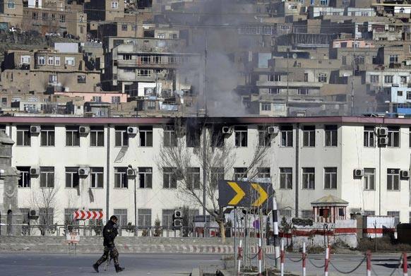 An Afghan security officers takes position, as smoke rises from the building of the Kabul traffic police headquarters in Kabul, Afghanistan.