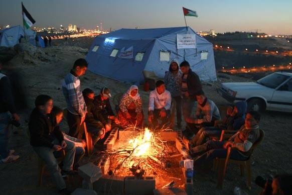 Palestinian activists sit by the fire in the village of Beit Iksa in the West Bank, between Ramallah and Jerusalem, seen in the background.