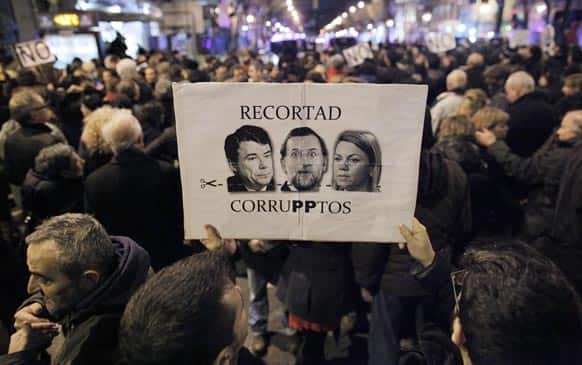 People hold a banner with pictures of Spanish Prime Minister Mariano Rajoy, and Popular Party`s members, María Dolores de Cospedal, and Luis Bracenas, ex treasurer, reading `let`s cut on corrupts` as they protest against corruption outside the Popular Party`s headquarters in central Madrid.