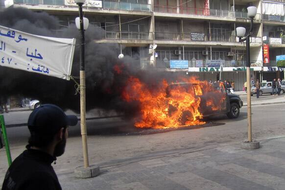 Lebanese residents watch a burning car that burst into flames when armed protesters attacked the convoy of a cabinet minister, in the northern city of Tripoli, Lebanon.