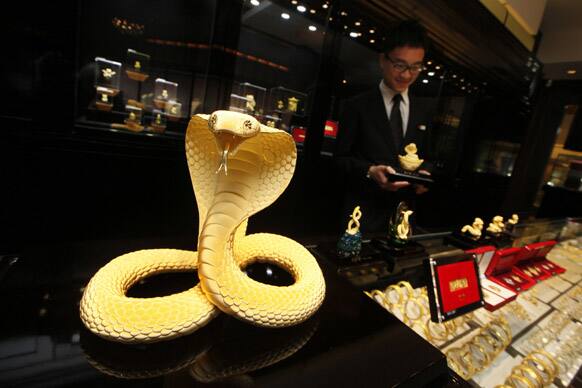An assistant shop clerk works near a newly unveiled gold snake on display for sale ahead of the upcoming Chinese lunar new year, the year of the Snake, at a jewelry shop in Hong Kong.