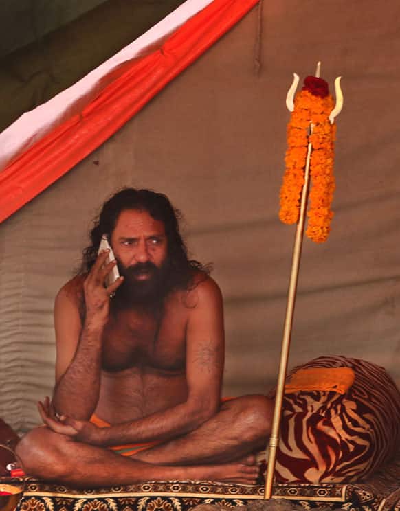 Hindu holy man talks on his mobile outside his camp at Sangam, the confluence of the Rivers Ganges, Yamuna and mythical Saraswati during the Maha Kumbh Mela, in Allahabad.