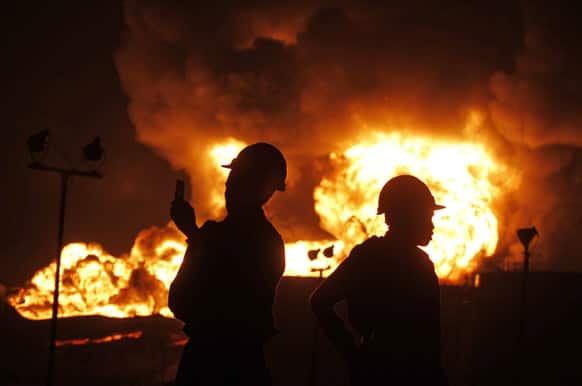 A firefighter takes photographs on a mobile phone as he stands with a colleague near flames rising from a storage tank of Indian Oil Corporation depot in Hajira, near Surat, in the western Indian state of Gujarat.