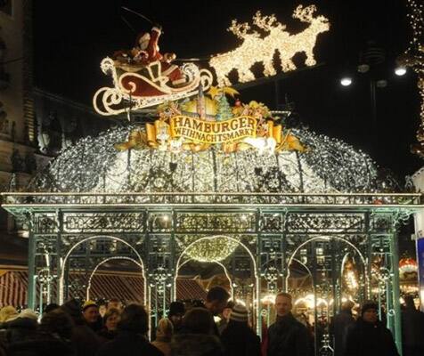 People stand in front the seasonal illuminated entrance of a Christmas market in front of Hamburg's Town Hall in Hamburg, Germany.