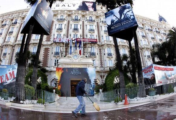 A worker sweeps in front of the Carlton hotel filled with movie billboards as preparations continue ahead of the 63rd Cannes Film Festival in Cannes