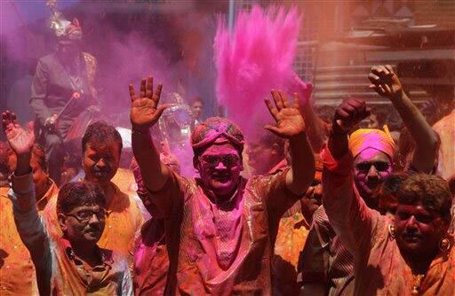 Indians smeared with colored powder dance during Holi festivities in Hyderabad.