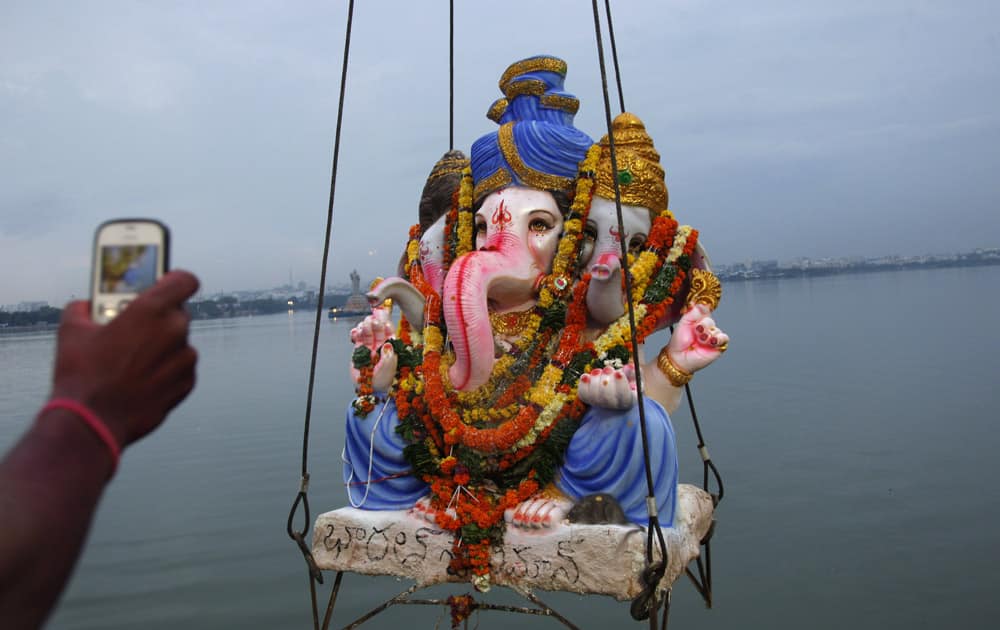 A devotee takes a picture of an idol of elephant-headed Hindu god Ganesha as it is lifted to be immersed in the Hussain Sagar Lake during Ganesh Chaturthi festival celebrations in Hyderabad.