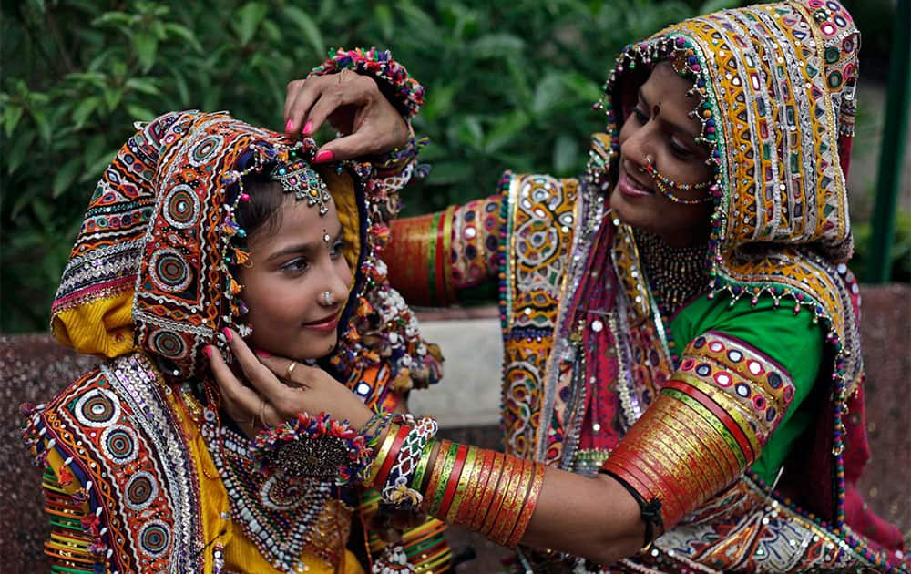 A woman, dressed in traditional finery, helps a girl with her costume before practicing the Garba dance ahead of the Navratri festival in Ahmadabad.