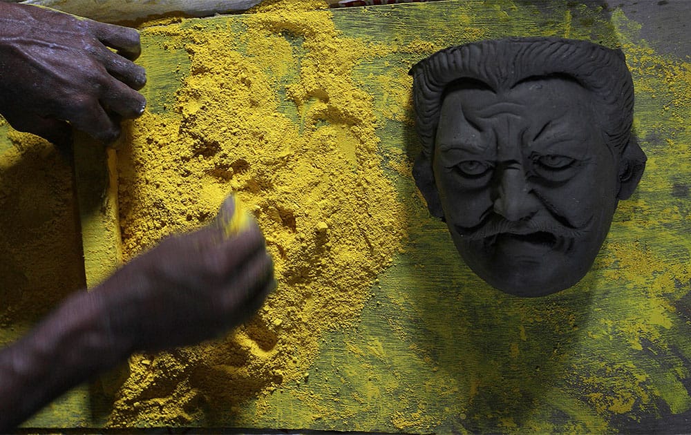 An artisan mixes colors next to a demon face to paint idols of Hindu goddess Durga ahead of Durga Puja festival in Gauhati.