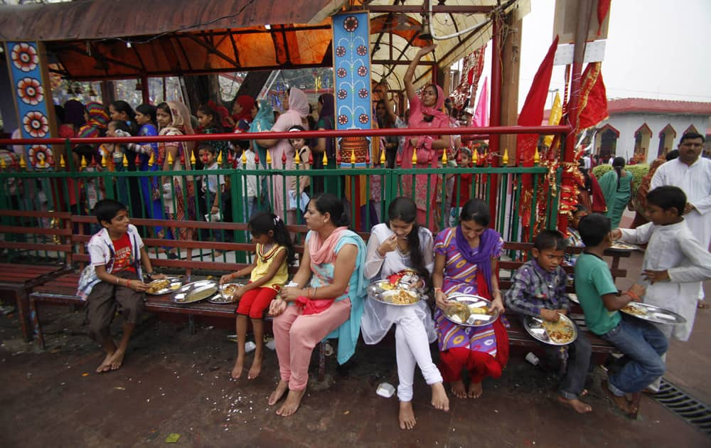 Hindu devotees eat holy food as others stand in a queue to offer prayers at a Hindu goddess Kali temple on the second day of the Navratri festival in Jammu.