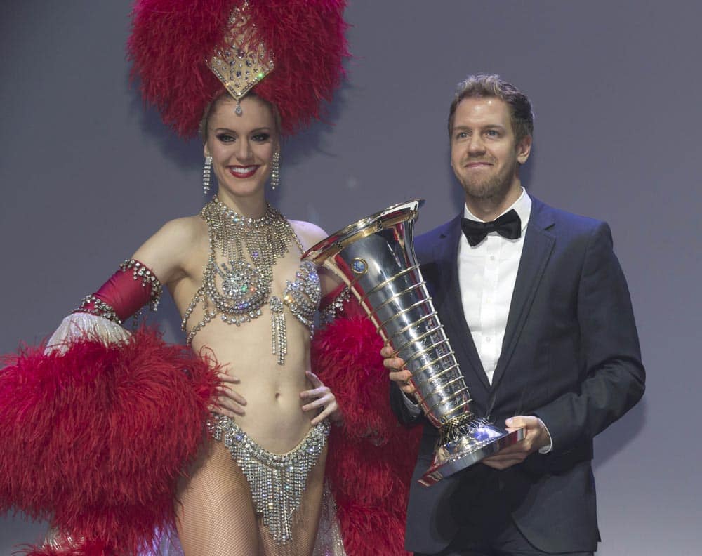 2013 Formula One world champion Sebastian Vettel of Germany holds his trophy next to a Moulin Rouge dancer during the FIA Prize-Giving gala in Saint Denis, outside Paris.