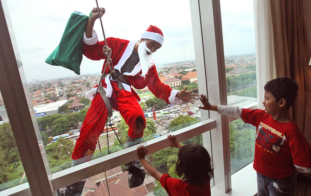 An employee in Santa outfit greets children as he rappels down from the roof of a hotel during a promotional event to celebrate Christmas in Surabaya, East Java, Indonesia.