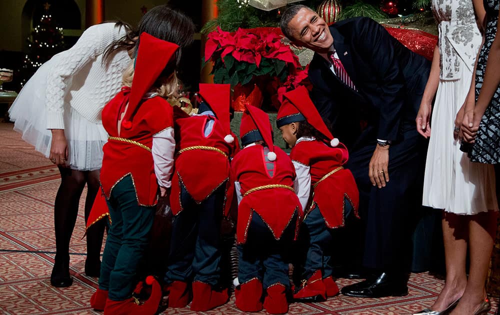 President Barack Obama, laughs as children dressed like elves gathered around a Christmas tree, look at their presents presented to them by the first family at the National Building Museum in Washington.