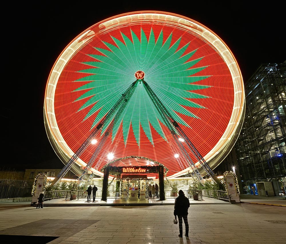 A woman watches an illuminated rotating Ferris wheel at a Christmas market in Essen, Germany.