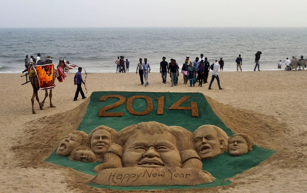 People walk near the sand sculpture to celebrate the new year 2014 created by sand artist Sudarshan Pattnaik at the Puri sea beach, 67 kilometers away from the eastern Indian city of Bhubaneswar.
