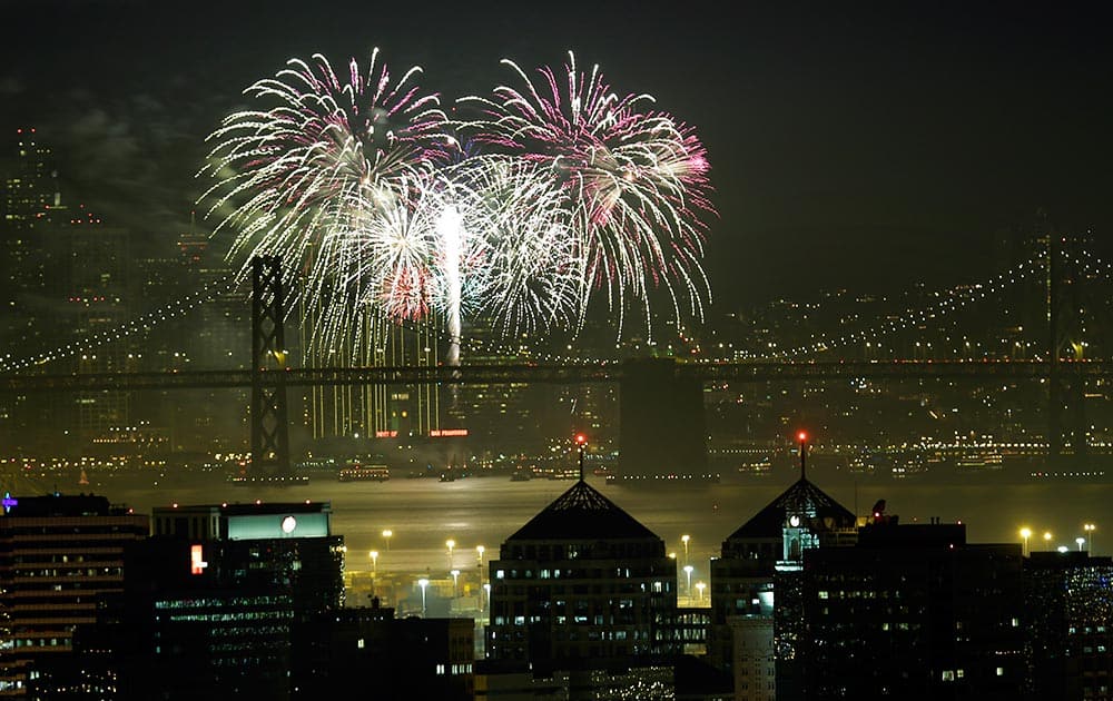 Fireworks fill the air in the bay over the Oakland, bottom, and San Francisco skylines, divided by the San Francisco Oakland Bay Bridge, as part of New Year's Eve celebrations in a view from Oakland, Calif.