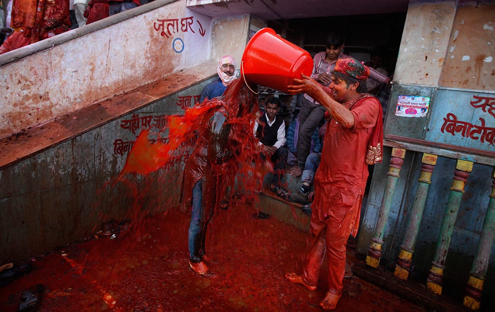 A Hindu man pours a bucket of colored water on a woman outside the Ladali or Radha temple before the procession for the Lathmar Holi festival, the legendary hometown of Radha, consort of Hindu God Krishna, in Barsana.