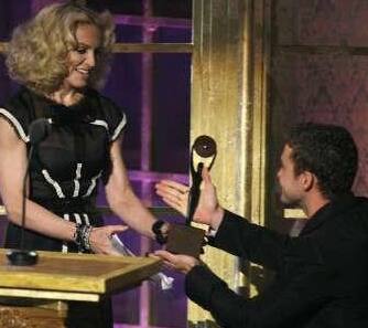 Justin Timberlake (R) kneels as he presents singer Madonna with her award during her induction at the 23rd annual Rock and Roll Hall of Fame.