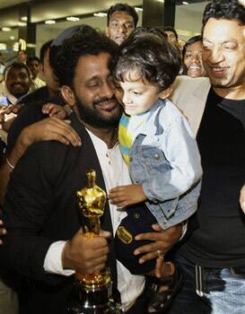 Oscar award winner Resul Pookutty, left, holding the Oscar statuette, hugs an unidentified child as actor Irrfan Khan, right, looks on after they arrived at the international airport in Mumbai.