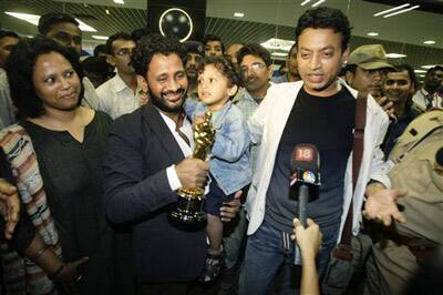 Oscar award winner Resul Pookutty, left, holding the Oscar statuette, hugs an unidentified child as actor Irrfan Khan, right, looks on after they arrived at the international airport in Mumbai.